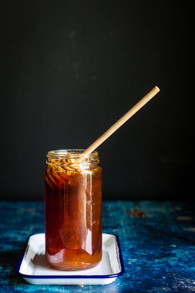 Picture of a glass jar of honey with a honey ladle in it. 